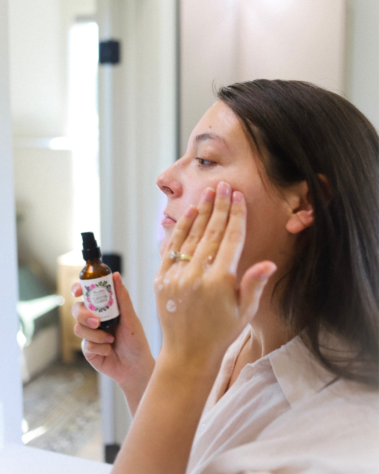 A profile shot of a woman holding the Clarifying Cleanser while rubbing it onto her face.